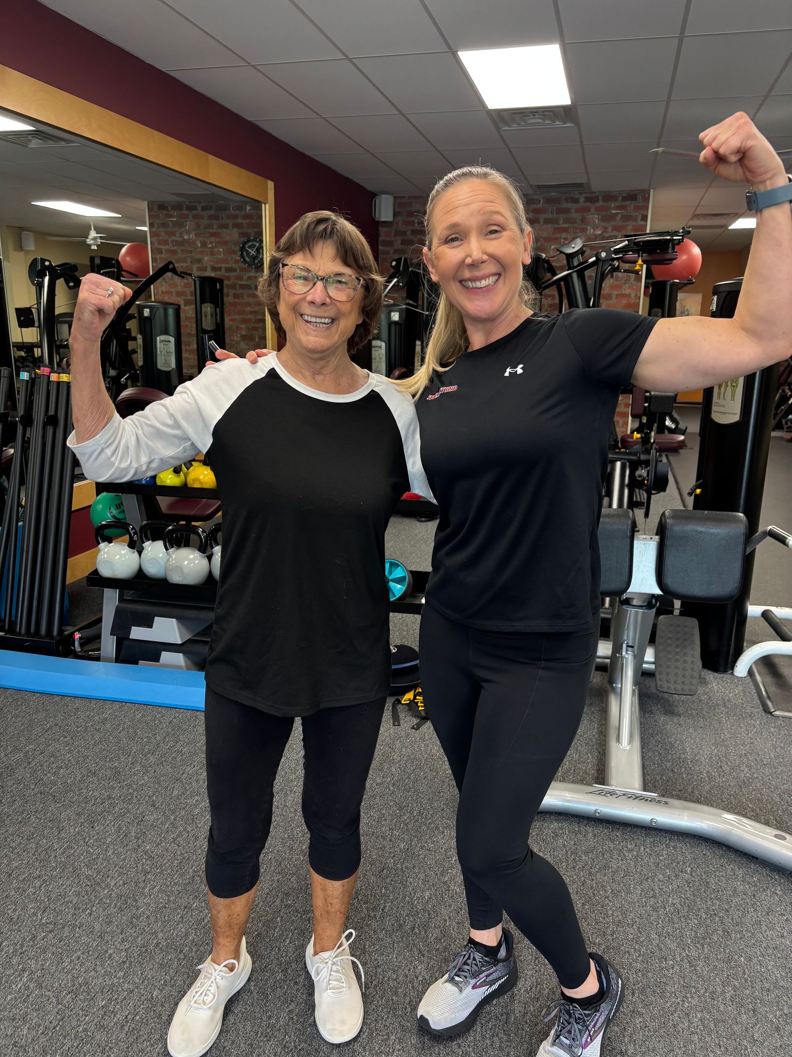 A member and her trainer flex side by side, cheek to cheek
