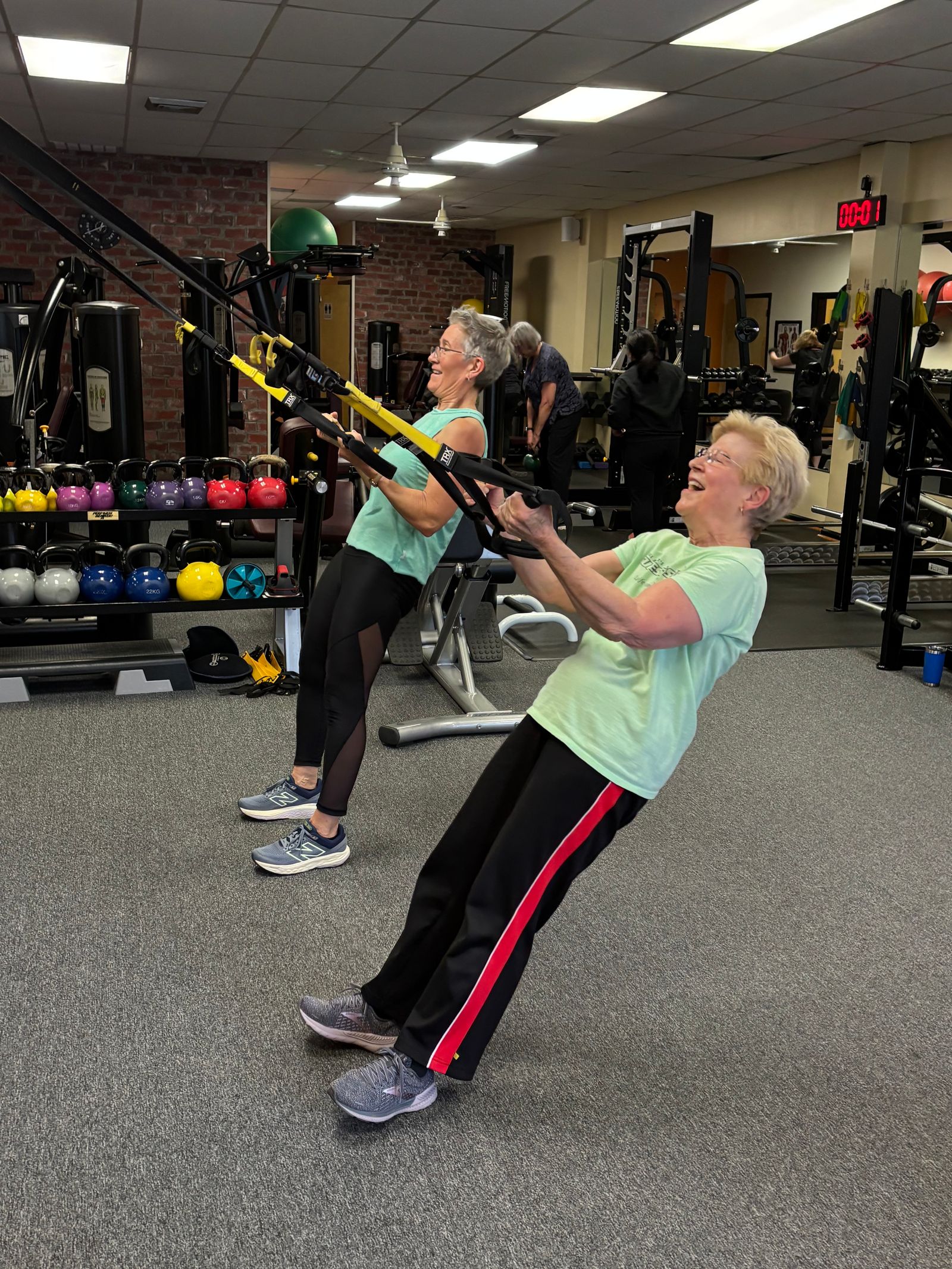 Two members laugh as they lean back into suspension-trainer rows