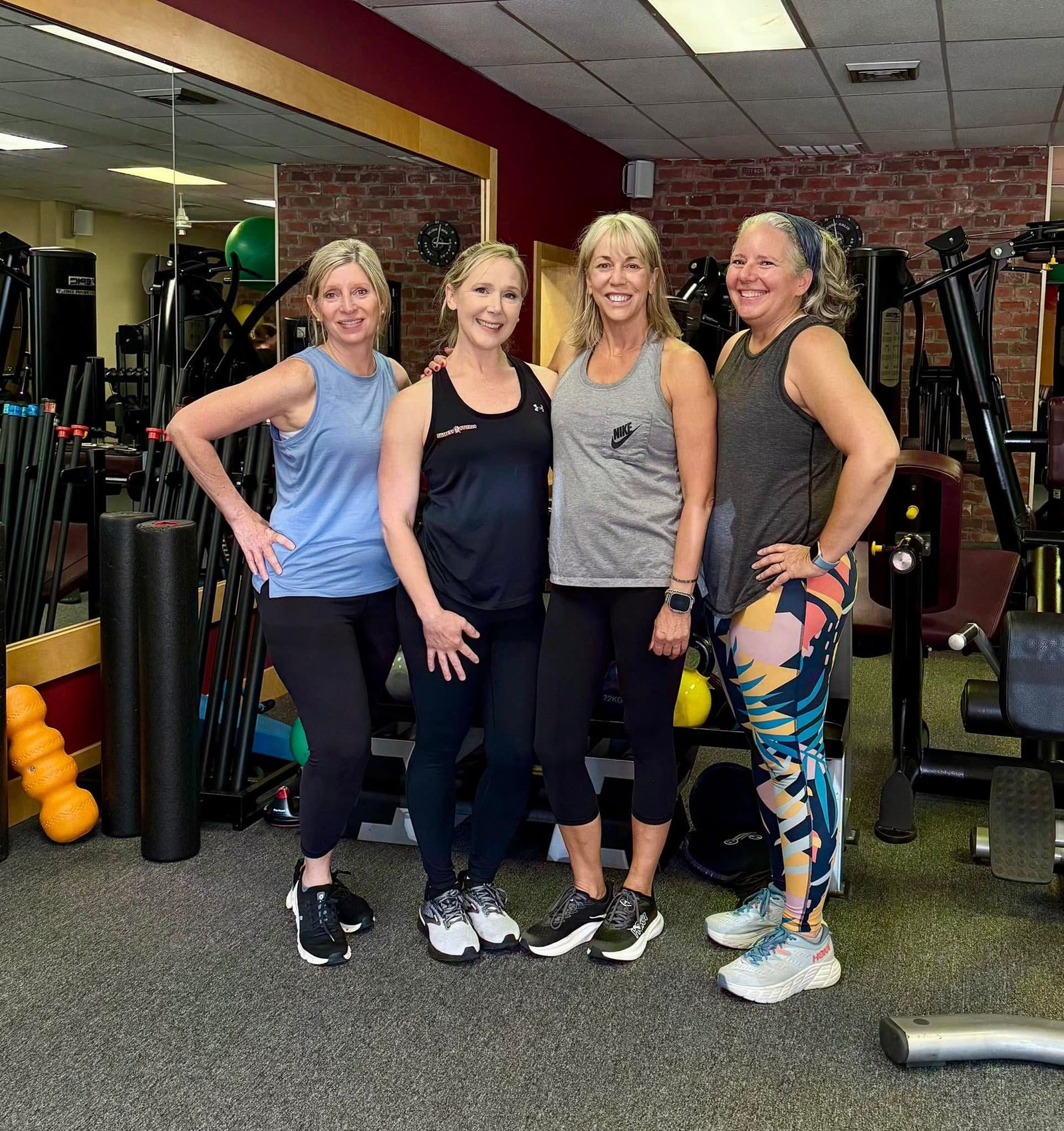 Four members stand together, smiling, in the brick-walled weight room