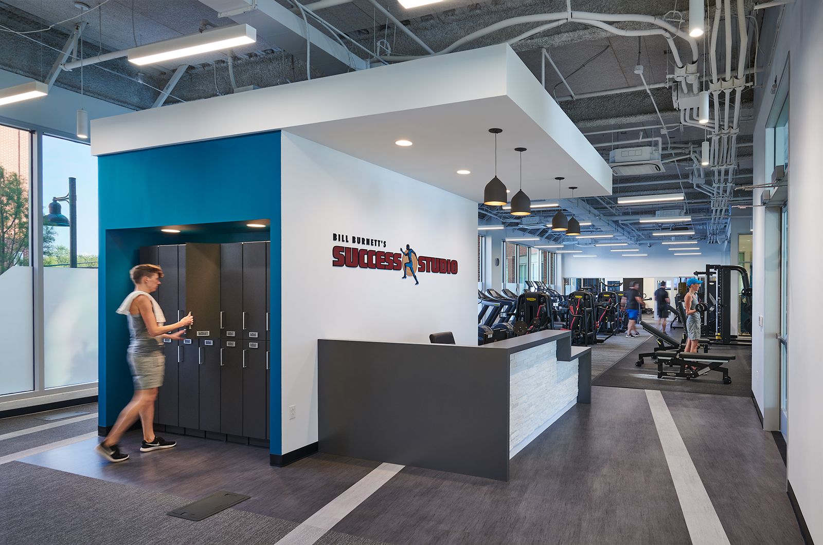 The North lobby: the front desk under the Bill Burnett’s Success Studio wall logo, the training floor beyond