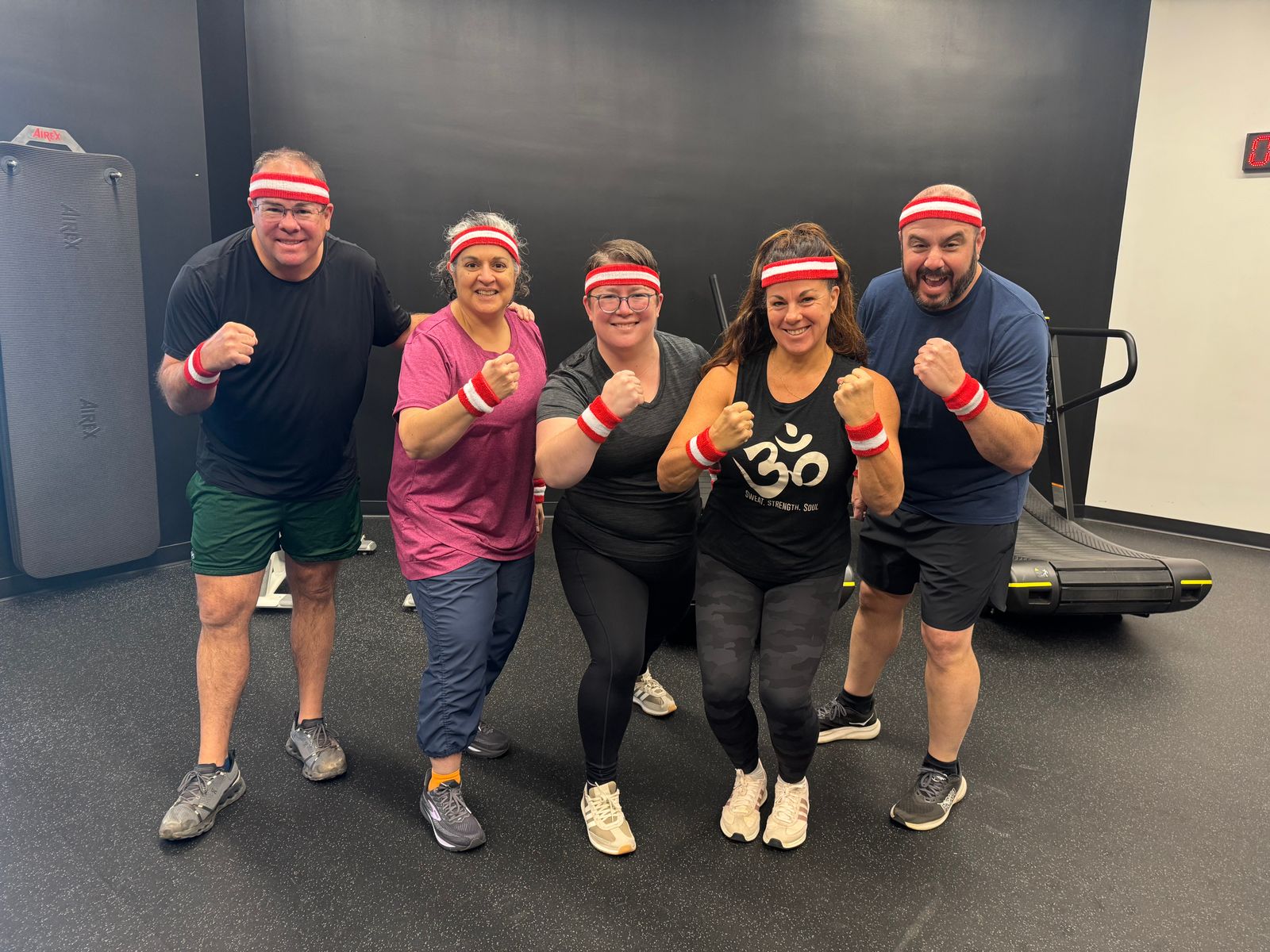 Five members in matching red-and-white sweatbands raise their fists in the group studio