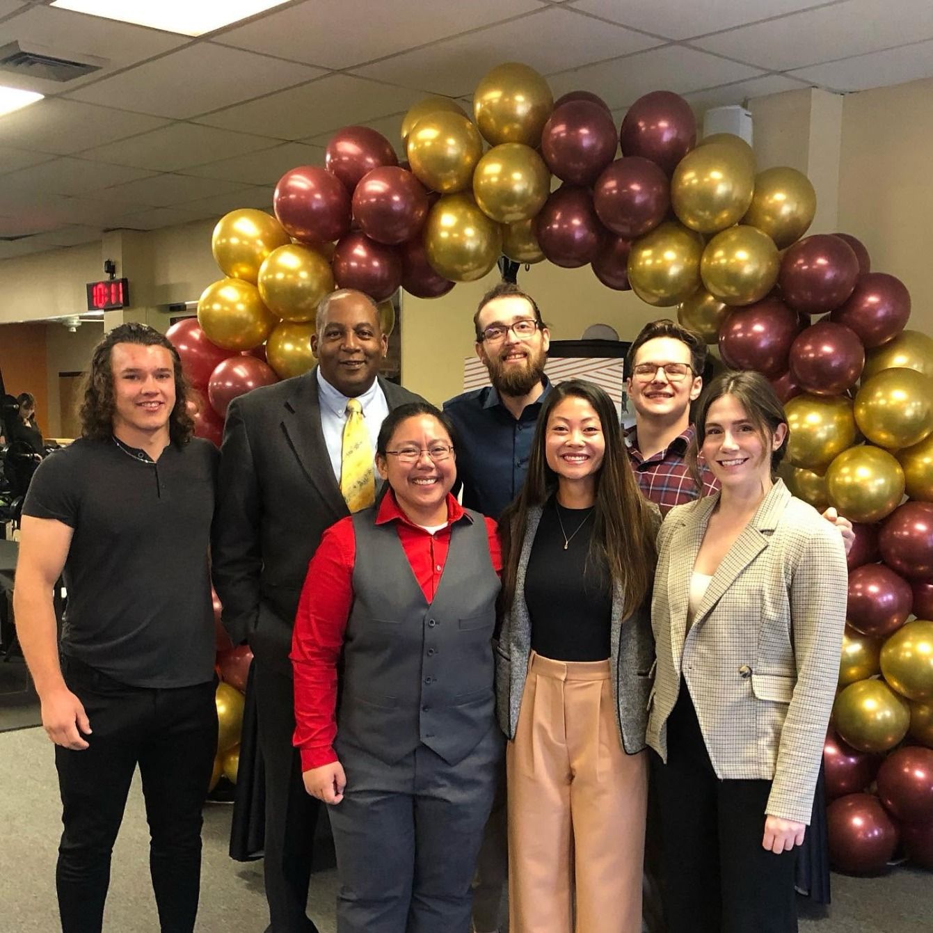 The Success Studio team in dress clothes under a maroon and gold balloon arch
