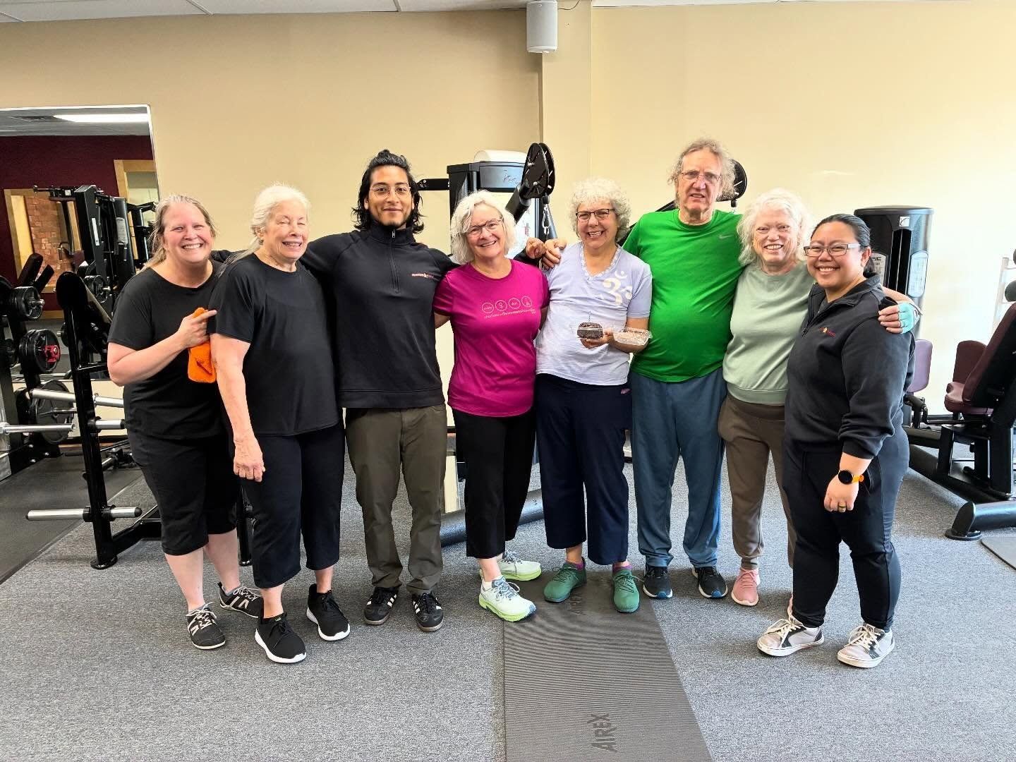 Eight members and trainers stand arm in arm in the studio