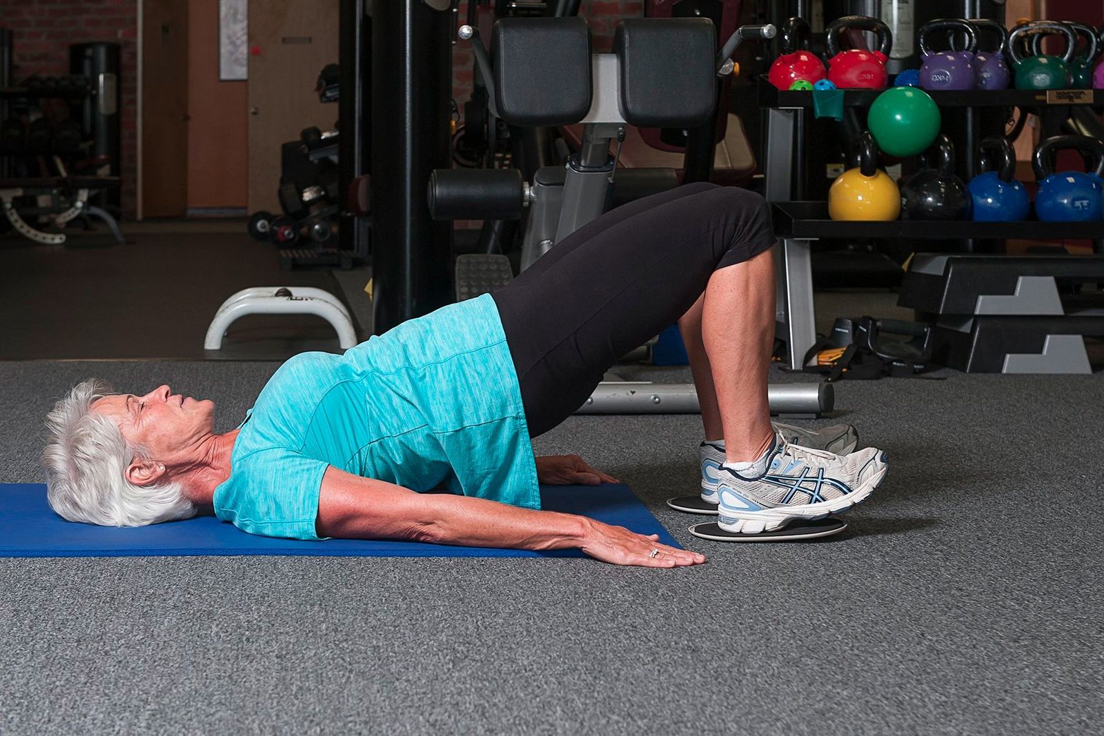A woman holds a glute bridge on a mat, a slider under her feet
