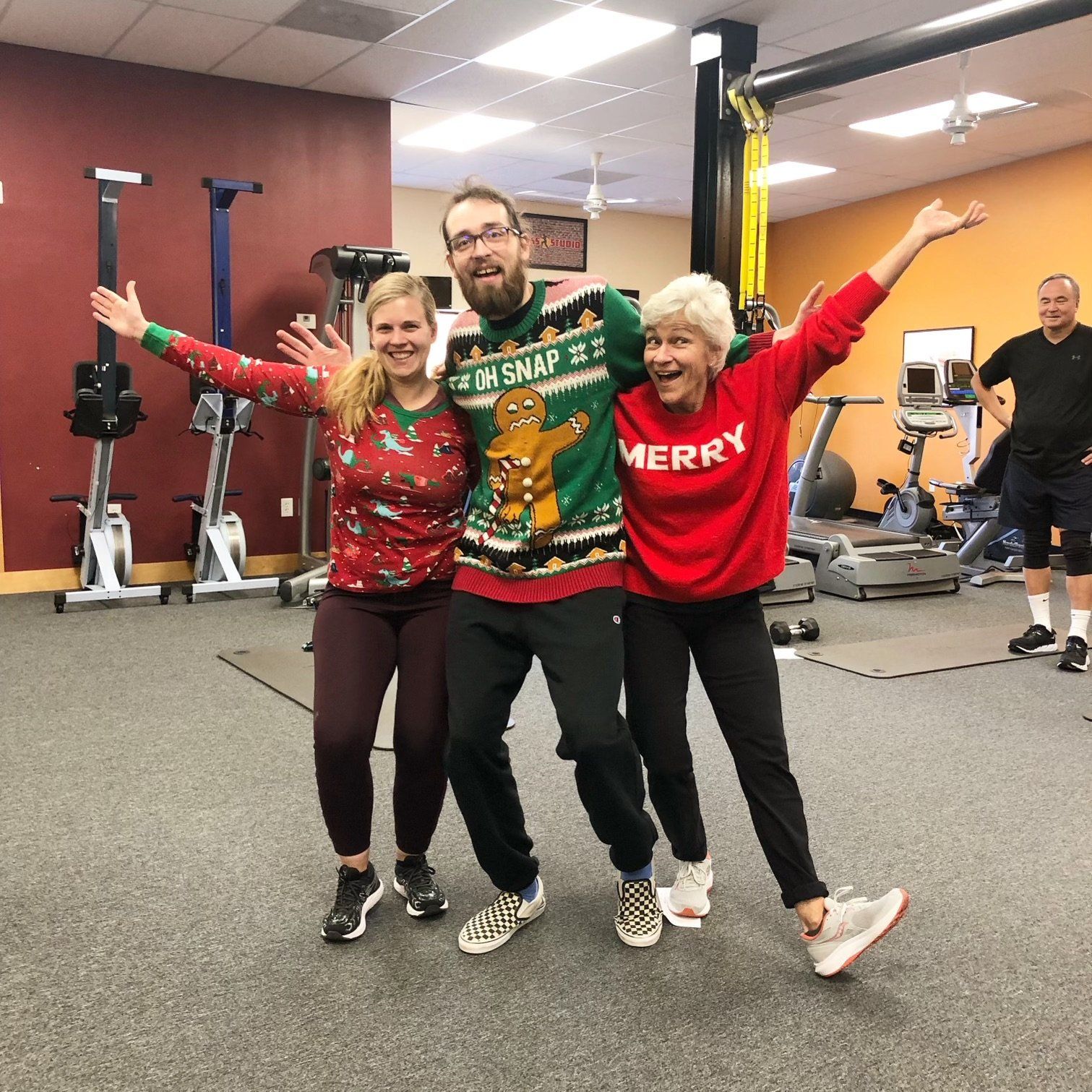 Three members in holiday sweaters throw their arms wide in the studio